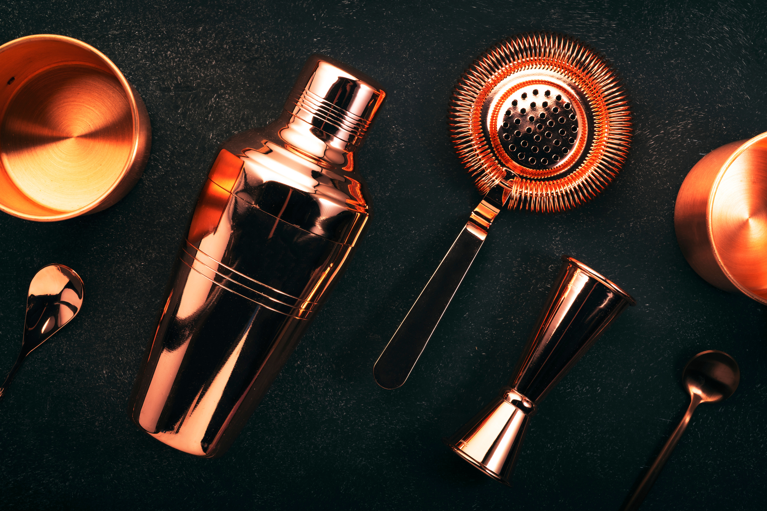 Copper bar tools and bartender accessories for making cocktail. Shaker, jigger, strainer, spoon. Alcohol drinks and beverages preparation. Black background, top view